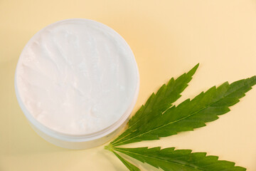Cosmetic hemp oil. Marijuana leaf with one jar of cosmetic cream with open lid.