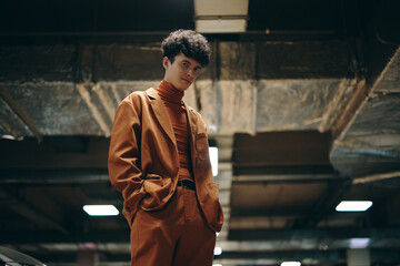 Young man in stylish brown outfit standing confidently in a modern parking garage