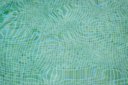 blue water background of crystal clear swimming pool floor and tiles distorted by breaking light