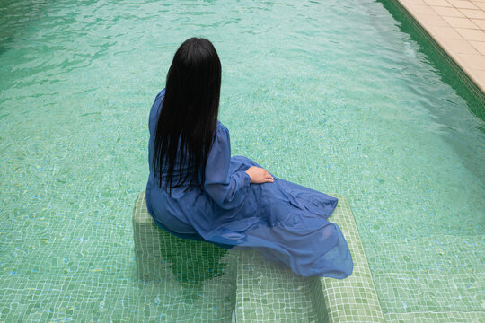 art portrait of woman in blue dress relaxing in swimming pool as seen from behind