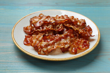 Slices of tasty fried bacon on light blue wooden table