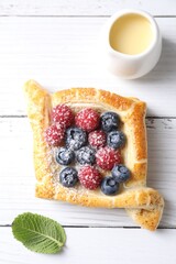 Tasty puff pastry with berries on white wooden table, top view