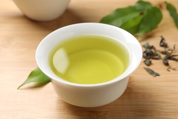 Refreshing green tea in cup and leaves on wooden table, closeup