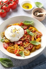 Delicious fresh burrata salad in bowl and ingredients on light gray textured table, closeup
