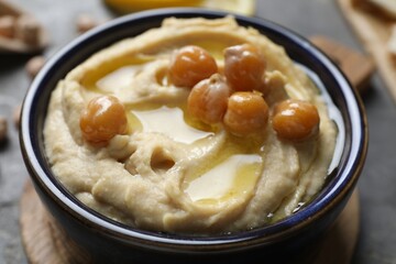 Delicious hummus with olive oil and chickpeas in bowl on grey table, closeup