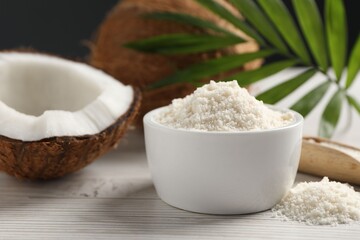 Fresh coconut flour in bowl, nuts and palm leaf on white wooden table