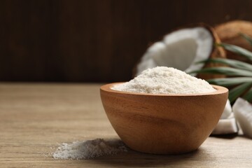 Fresh coconut flour in bowl, nut and palm leaf on wooden table, space for text