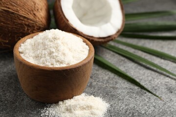 Organic coconut flour in bowl, fresh fruits and leaf on grey table, closeup