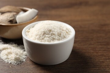 Organic coconut flour in bowl on wooden table, closeup
