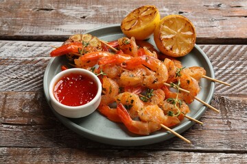 Delicious grilled shrimp skewers served with sauce and lemon on wooden table