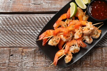 Delicious grilled shrimp skewers served with sauce and lime on wooden table, top view. Space for text