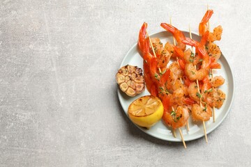 Delicious grilled shrimp skewers, lemon and garlic on light grey table, top view. Space for text