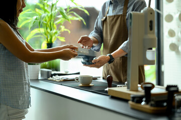Female customer tapping credit card on a contactless payment terminal at modern coffee shop