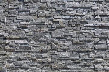 Stone coating wall made of striped stacked bricks of natural gray rocks. External wall covering,...