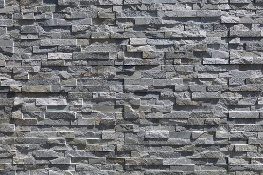 Fototapeta Stone coating wall made of striped stacked bricks of natural gray rocks. External wall covering, background and texture. 