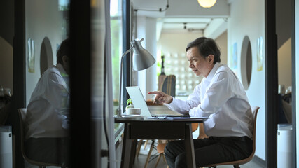 Smiling middle age businessman in white shirt working in a modern office environment