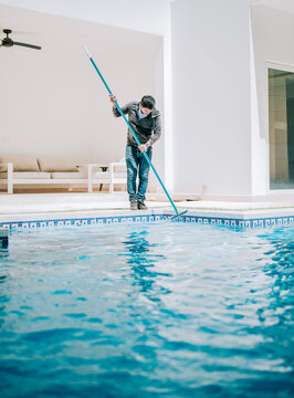 Male worker cleaning a home swimming pool with special brush. Home pool cleaning with wall brush