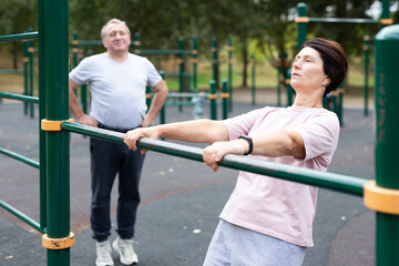 Elderly woman doing exercises on sports bars at outdoor sports ground