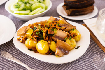 Baked potatoes with chanterelles and bacon served with herbs and lightly salted cucumbers on table