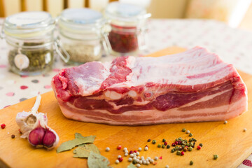 Fresh piece of pork belly on wooden board with spices