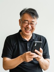 A middle-aged Asian man smiling at his phone, against a white background. 