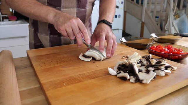 Preparing shallots by slicing them on a wooden board. Male hands with a knife, under natural light in a genuine kitchen.