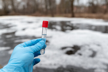 Test tube with water inside in hand of a person, close up. Foam on water surface on the background,...