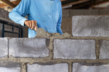 Construction workers are building cement walls with brick blocks.