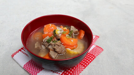 Sup daging, clear soup with beef slices, corn and vegetables. Served in bowl on grey background. Selected focus