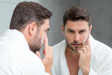 Fototapeta premium Skin care. Beauty middle aged man applying face cream. Male spa hold face cream. Facial cream, moisturizing lifting nourishing creme. Face cream for skincare. Wrinkle cosmetic facial treatment.
