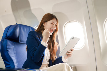 Fototapeta premium An Asian businesswoman takes a plane ride near the window to study abroad. She reads a book, looks out the window, uses her computer, smiles, and feels happy during the flight.