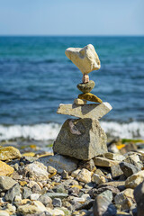 Balanced stone tower stands precariously on rocky beach, with blue ocean and foamy waves in the...