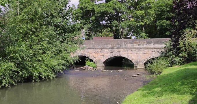 Slow motion footage of the beautiful town of Bedale, which is a market town and civil parish in North Yorkshire, England showing a beautiful river beck and the main bridge in the summer time