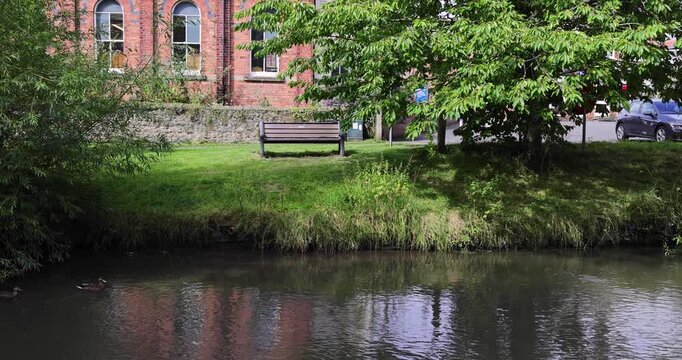 Footage of the beautiful town of Bedale, which is a market town and civil parish in North Yorkshire, England showing a beautiful bench by the river beck in the summer time