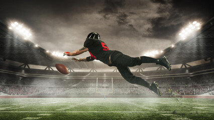 Focused and determined American football player in motion on open air arena, catching ball under...