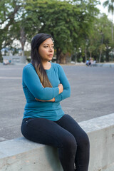 Woman sitting in a public park with her arms crossed in a worried, thoughtful attitude.