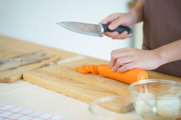 Closeup hands of asian women chopping slices carrot with knife on cutting board to preparing fresh vegetables of ingredients for cooking breakfast meal while making healthy food lifestyle in kitchen