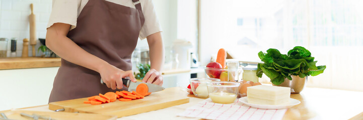 Closeup hands of asian women chopping slices carrot with knife on cutting board to preparing fresh vegetables of ingredients for cooking breakfast meal while making healthy food lifestyle in kitchen