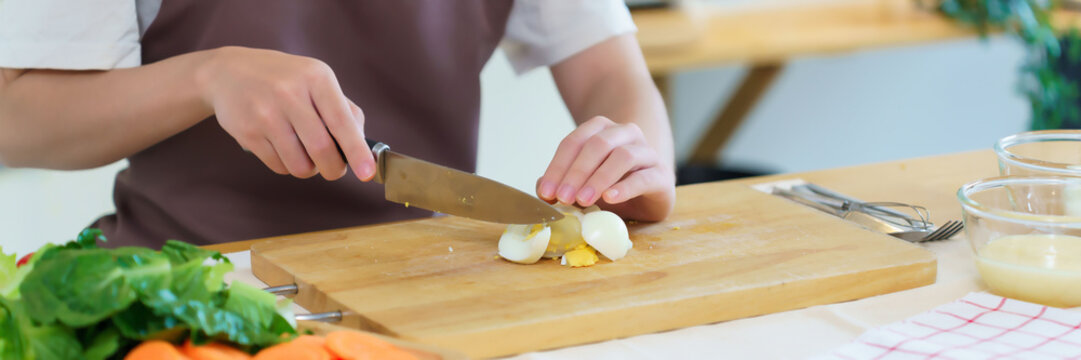 Closeup hands of asian women chopping boil egg with knife on cutting board and slice fresh vegetable to preparing ingredients for cooking breakfast meal while making healthy food lifestyle in kitchen - Powered by Adobe