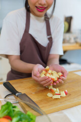 Asian women picking slices apple on cutting board into her hands to preparing fresh fruits of ingredients for cooking breakfast meal and salad while making healthy food lifestyle in kitchen at home