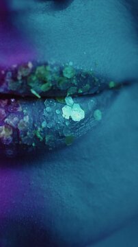 Close up beautiful sexy mouth girl. Beauty portrait of a face with lush lips of a woman. Healthy female with bright plum lipstick. There are glitter and sequins on the skin. Neon light in the studio