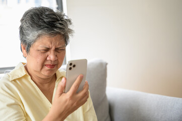 Senior people lifestyle health problem concept : Portrait photo of senior Asian woman has an eye long sighted problem trying to read message from smartphone monitor.