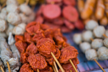 Various fried skewers meatballs and sausage. Selection of inexpensive street food skewers at market in Thailand