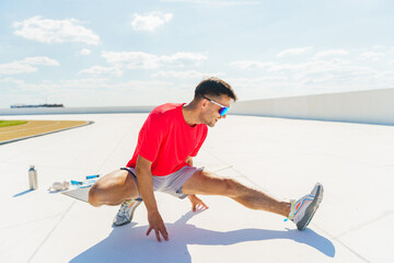 A man in a red shirt stretches his legs outdoors, focusing on his form under the bright sky.