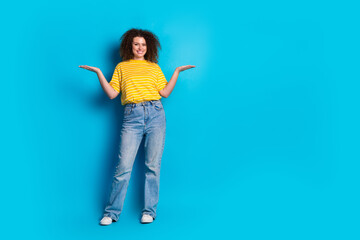 Full length photo of lovely young lady compare hold empty space dressed stylish striped yellow garment isolated on blue color background