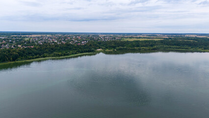 Drone photography of small town near lake surrounded by forest during summer day