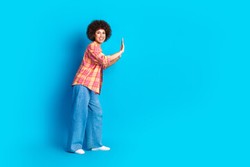 Full size photo of attractive young woman push wall empty space dressed stylish checkered clothes isolated on blue color background
