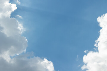 White clouds in a blue sky with sunbeams breaking through them