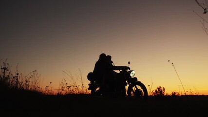 Silhouette of a young couple in love meets the sunset together sitting on a motorcycle