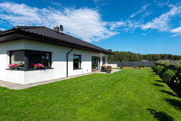 Obraz premium Beautiful garden with green grass, visible terrace table and house in beautiful summer weather, very wide shot.